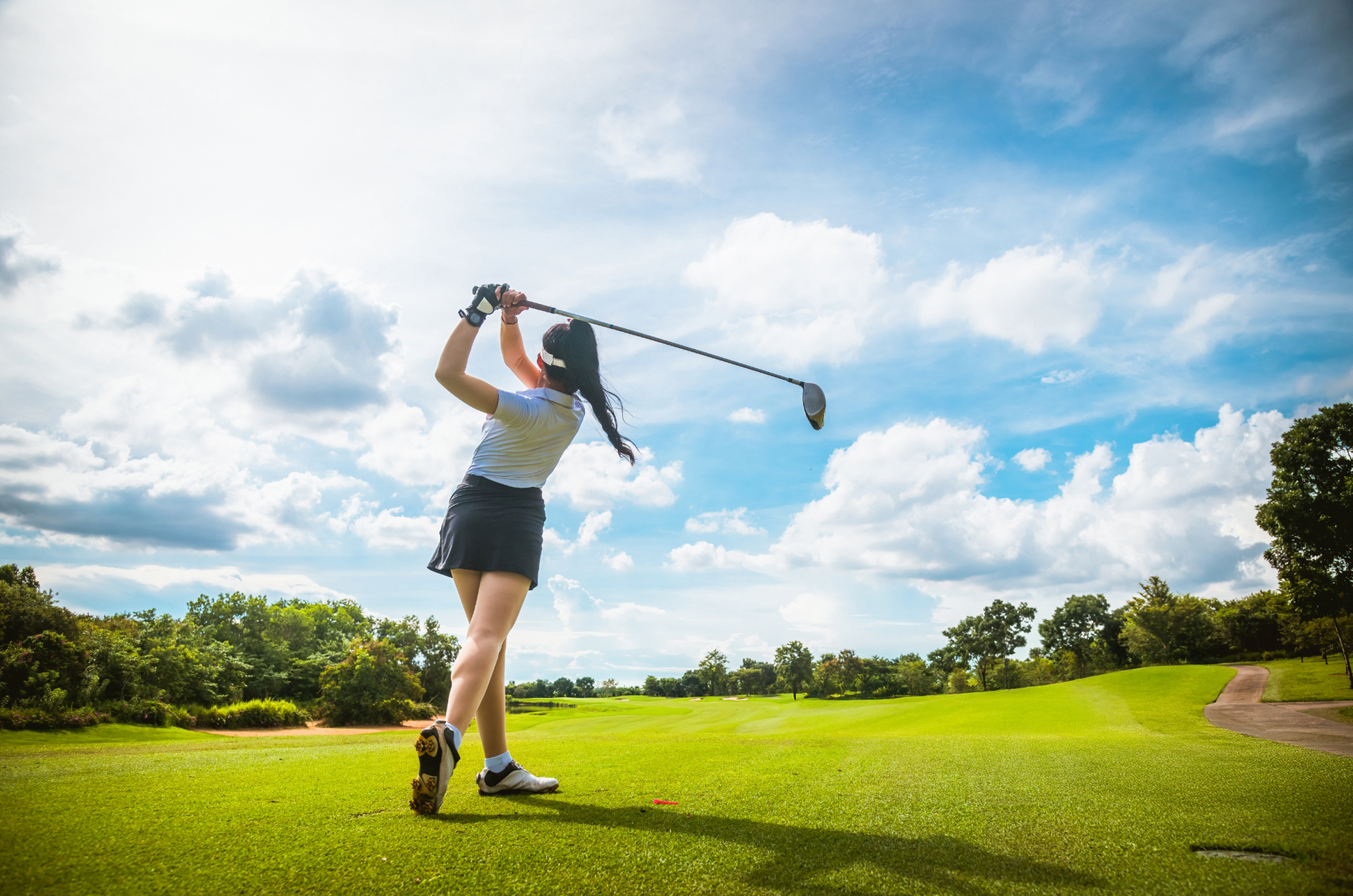 青空の下でドライバーショットを打つゴルファー